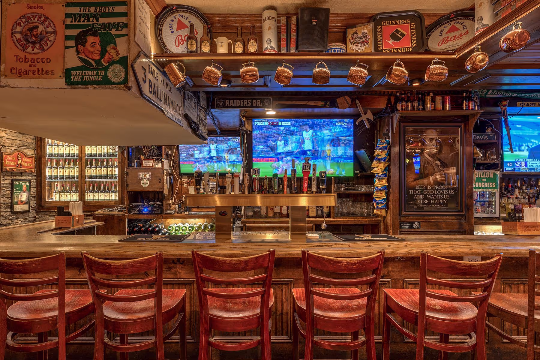 Empty wooden bar with red chairs, hanging mugs, beer taps, and sports playing on TVs behind the counter.